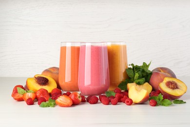 Fresh colorful fruit smoothies and ingredients on white table against wooden wall