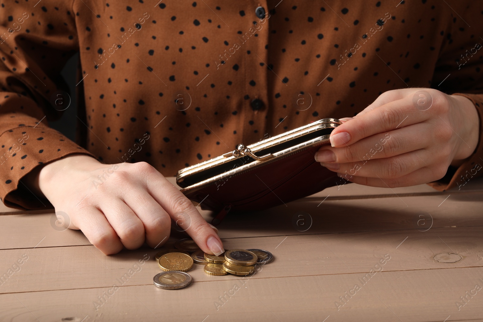 Photo of Poverty. Woman with wallet counting coins at wooden table, closeup