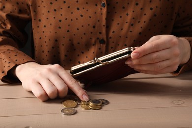 Photo of Poverty. Woman with wallet counting coins at wooden table, closeup