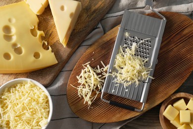 Grated, cut cheese and grater on wooden table, flat lay