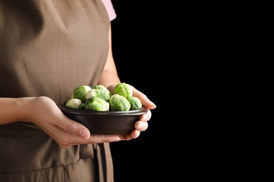 Photo of Woman holding bowl with Brussels sprouts on black background, closeup. Space for text