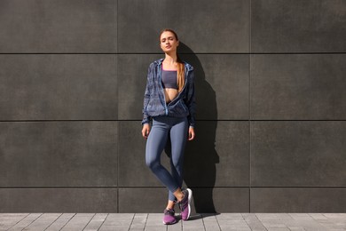 Beautiful woman in stylish gym clothes near dark grey wall on street
