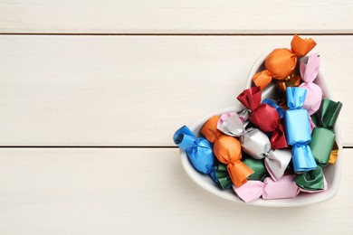 Photo of Candies in colorful wrappers on white wooden table, top view. Space for text