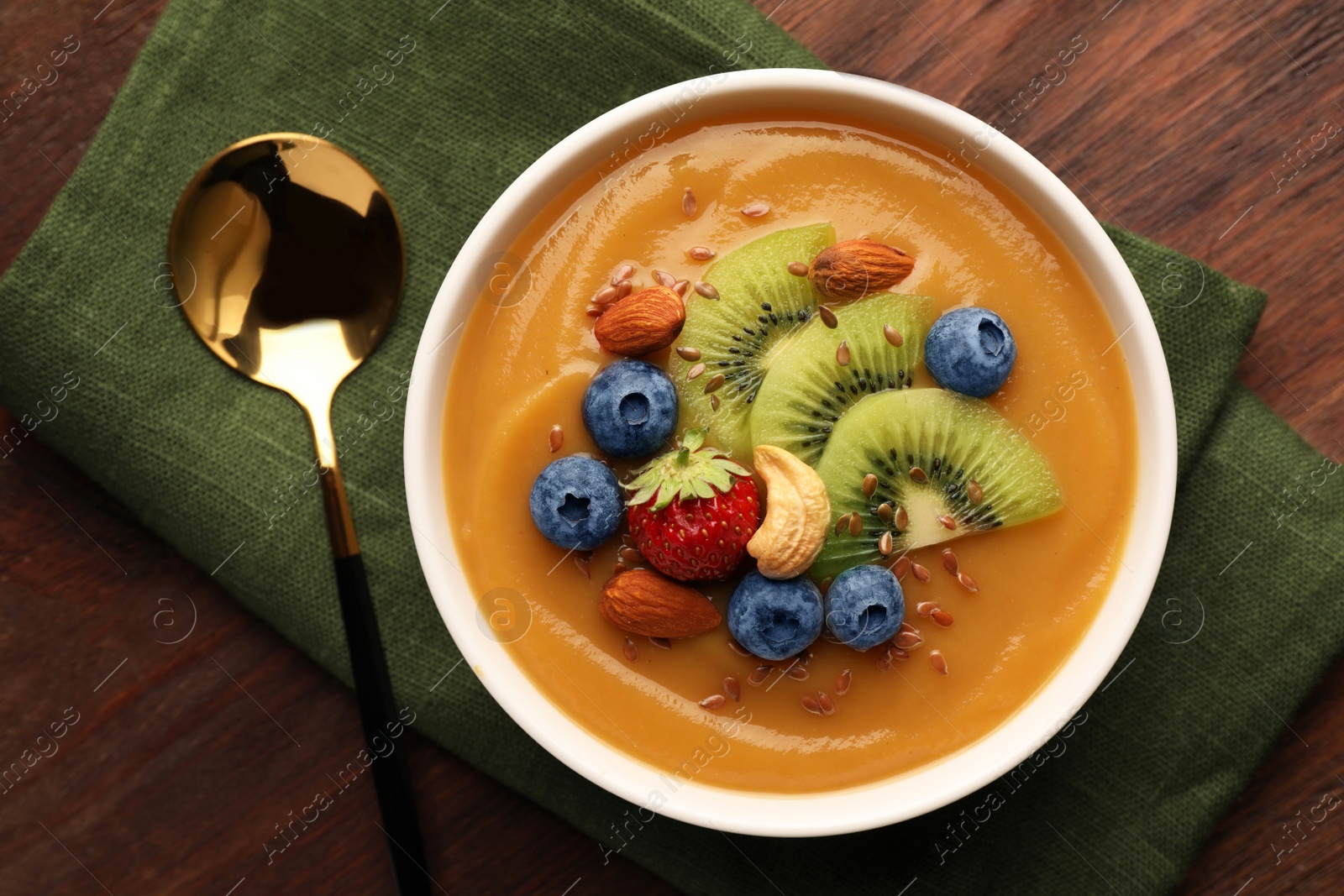 Photo of Delicious smoothie bowl with fresh berries, kiwi and nuts on wooden table, flat lay