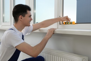 Photo of Worker using bubble level after plastic window installation indoors