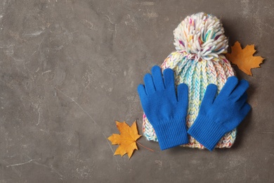 Photo of Stylish blue woolen gloves, hat and dry leaves on grey table, flat lay. Space for text