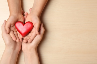 Photo of Woman and child holding heart on beige wooden background, top view with space for text. Donation concept