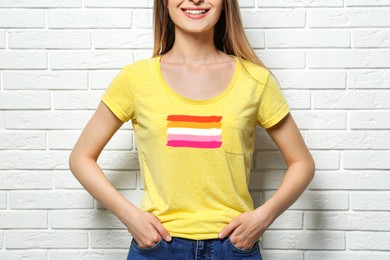 Image of Young woman wearing yellow t-shirt with lesbian flag near white brick wall. LGBT concept