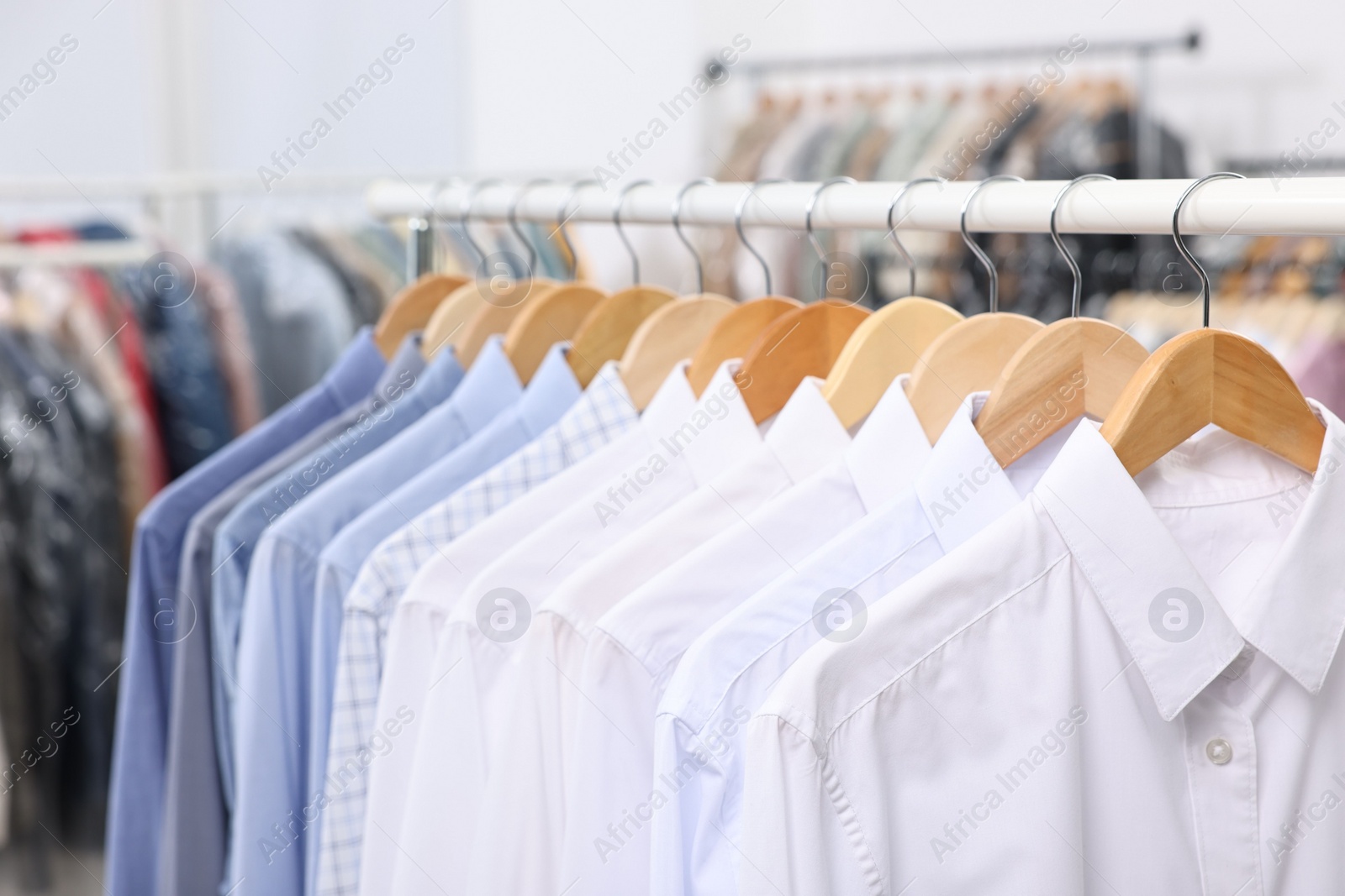 Photo of Dry-cleaning service. Many different clothes hanging on rack indoors, closeup