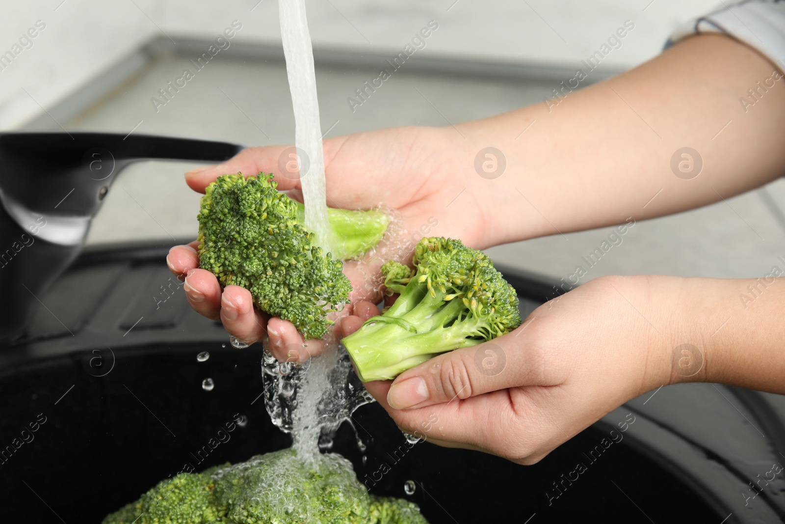 Photo of Woman washing fresh green broccoli in kitchen sink, closeup