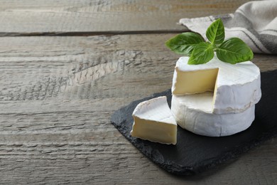 Photo of Tasty cut and whole brie cheeses with basil on wooden table, space for text