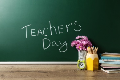 Photo of Green chalkboard with inscription TEACHER'S DAY and vase of flowers on wooden table