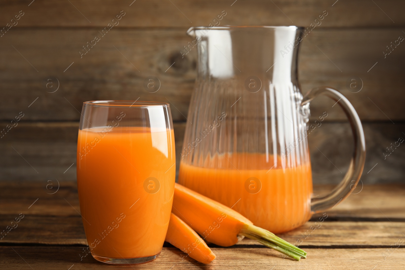 Photo of Jug and glass of freshly made carrot juice on wooden table