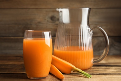 Photo of Jug and glass of freshly made carrot juice on wooden table