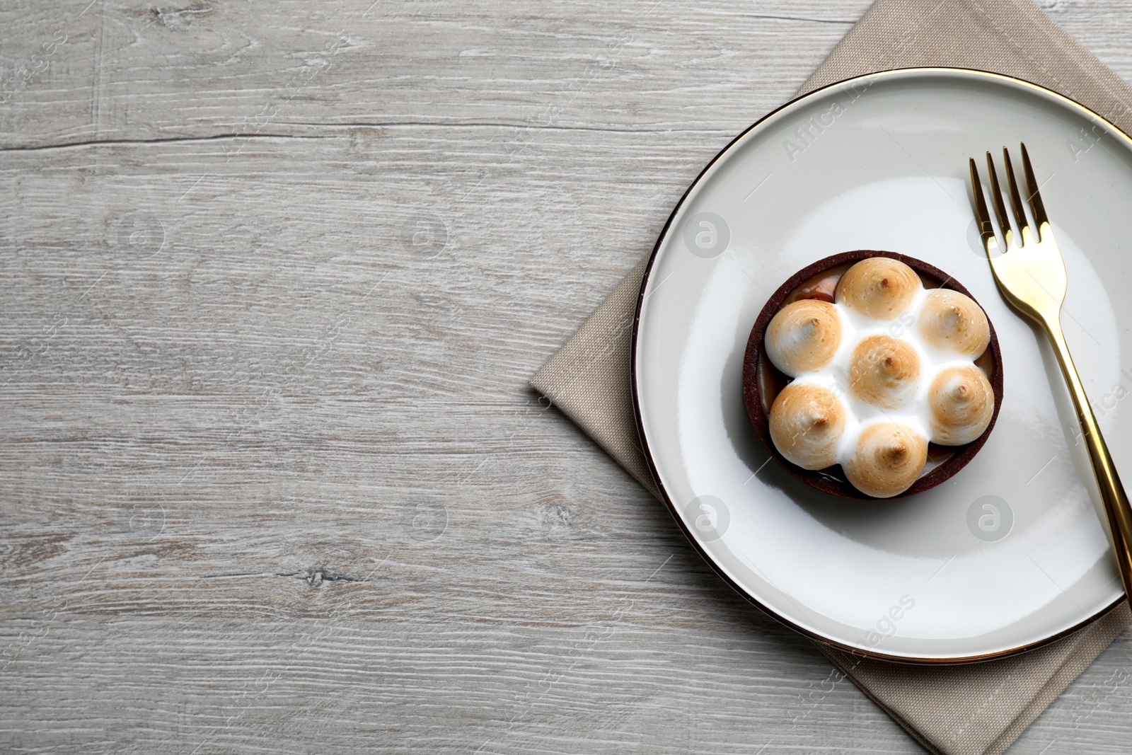 Photo of Delicious salted caramel chocolate tart with meringue served on light beige wooden table, top view. Space for text