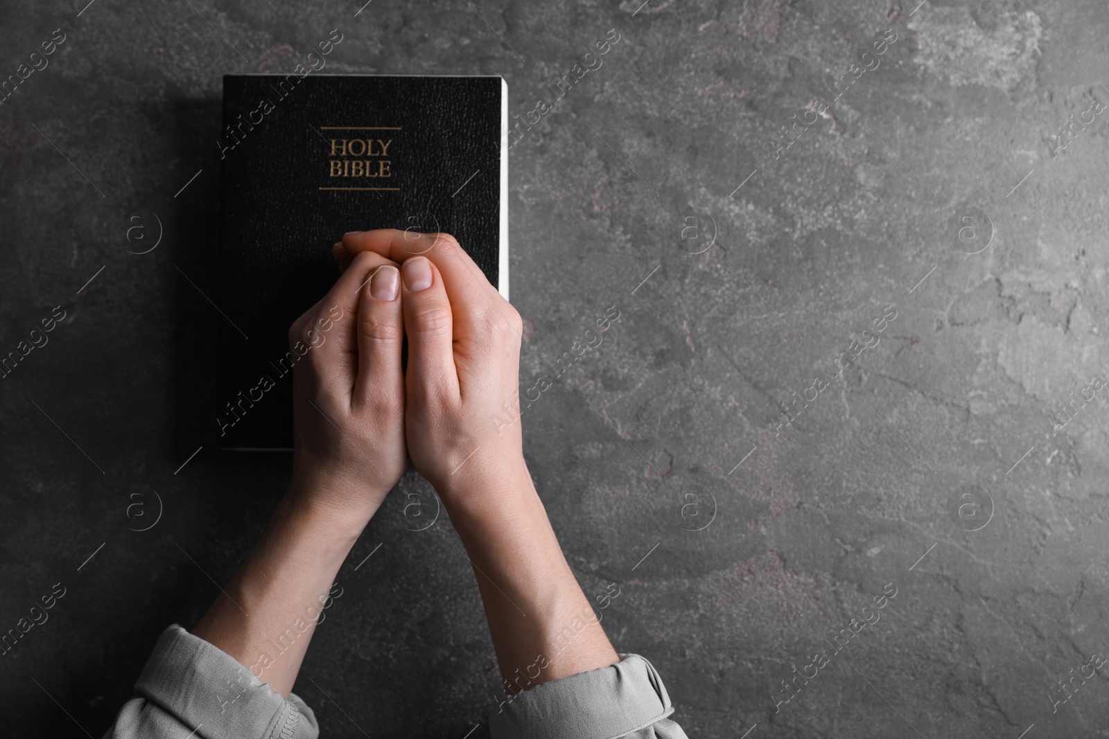 Photo of Religion. Christian woman praying over Bible at gray table, top view. Space for text