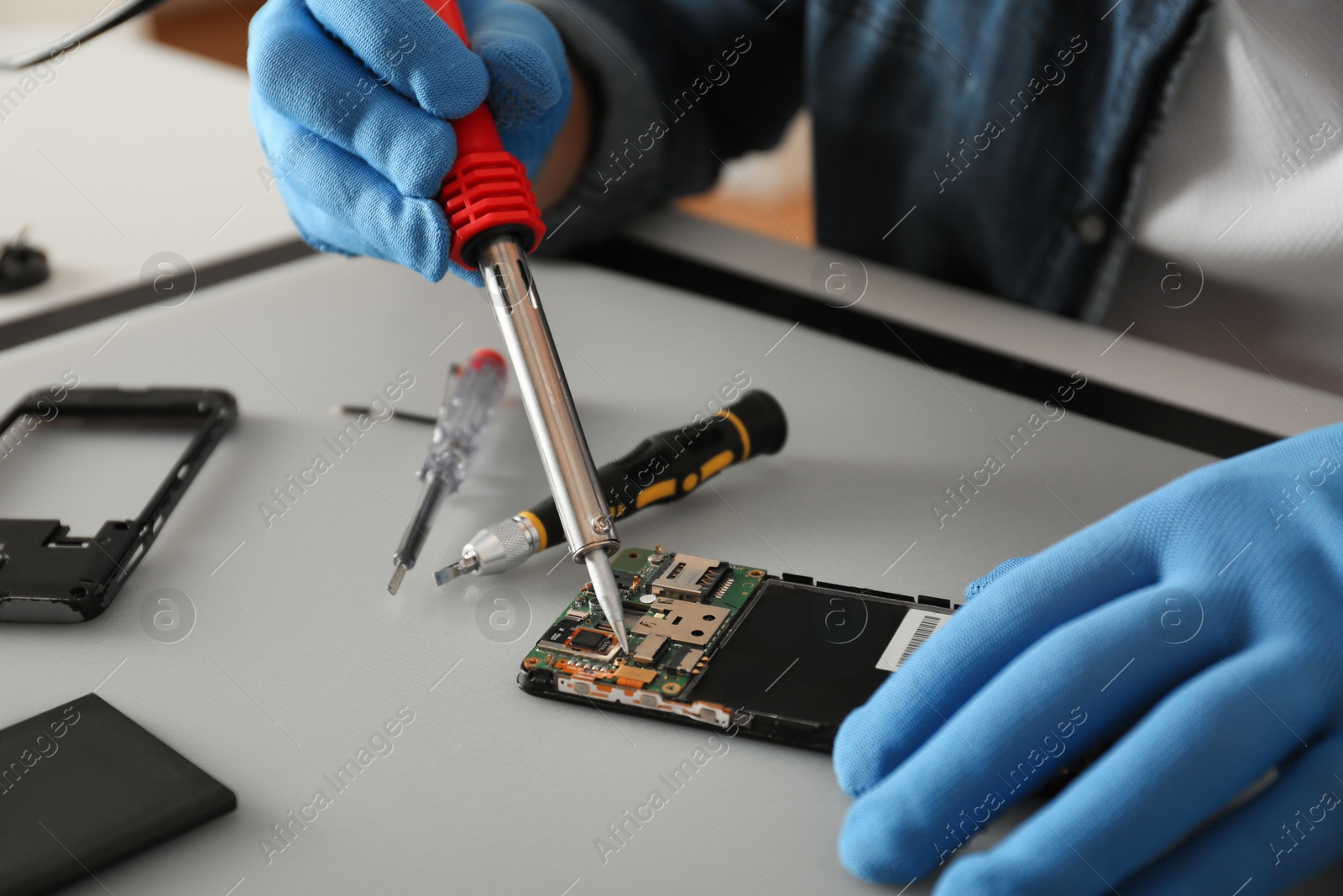 Photo of Technician repairing broken smartphone at table, closeup