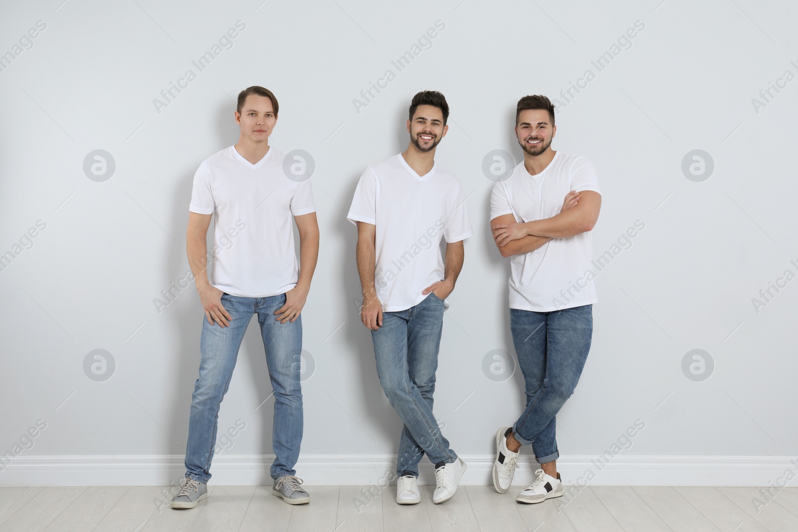 Photo of Group of young men in stylish jeans near light wall