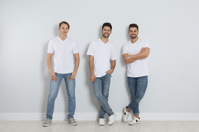 Group of young men in stylish jeans near light wall