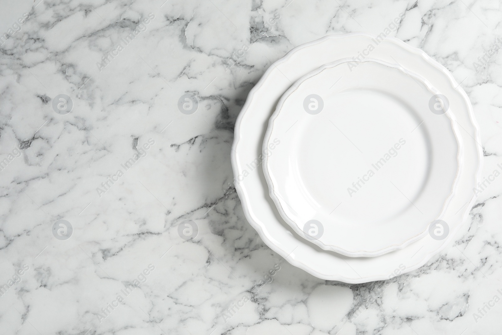 Photo of Empty ceramic plates on white marble table, top view. Space for text