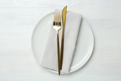 Stylish ceramic plate, cutlery and napkin on white wooden table, top view