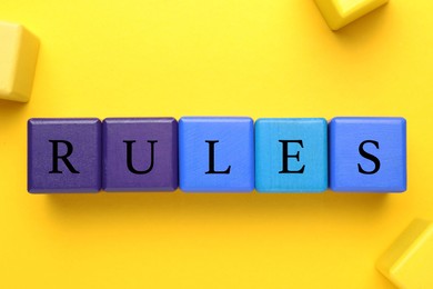 Photo of Word Rules made of colorful cubes with letters on yellow background, flat lay