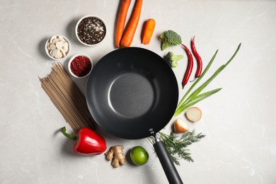 Photo of Empty iron wok surrounded by raw ingredients on light table, flat lay