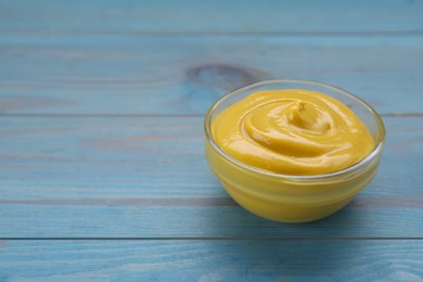 Photo of Sauce bowl with delicious mustard on light blue wooden table. Space for text