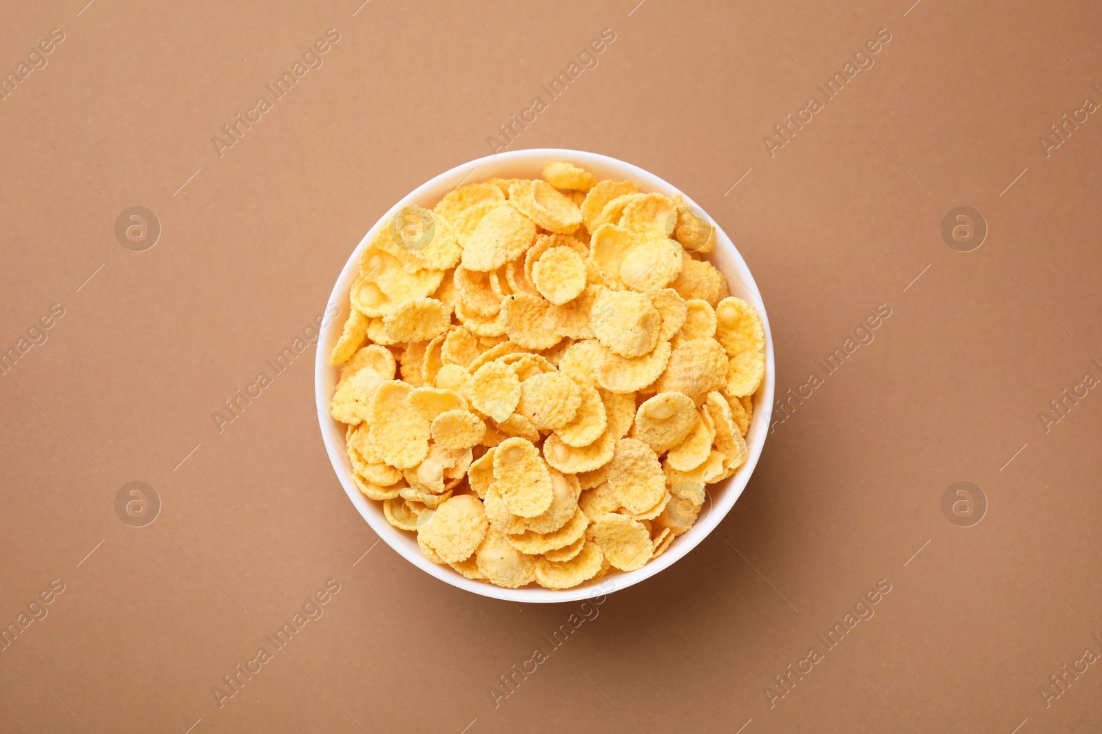 Photo of Breakfast cereal. Tasty corn flakes in bowl on brown table, top view