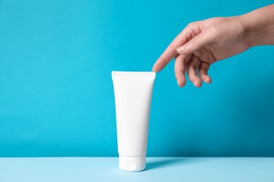 Photo of Woman with tube of hand cream at table against light blue background, closeup