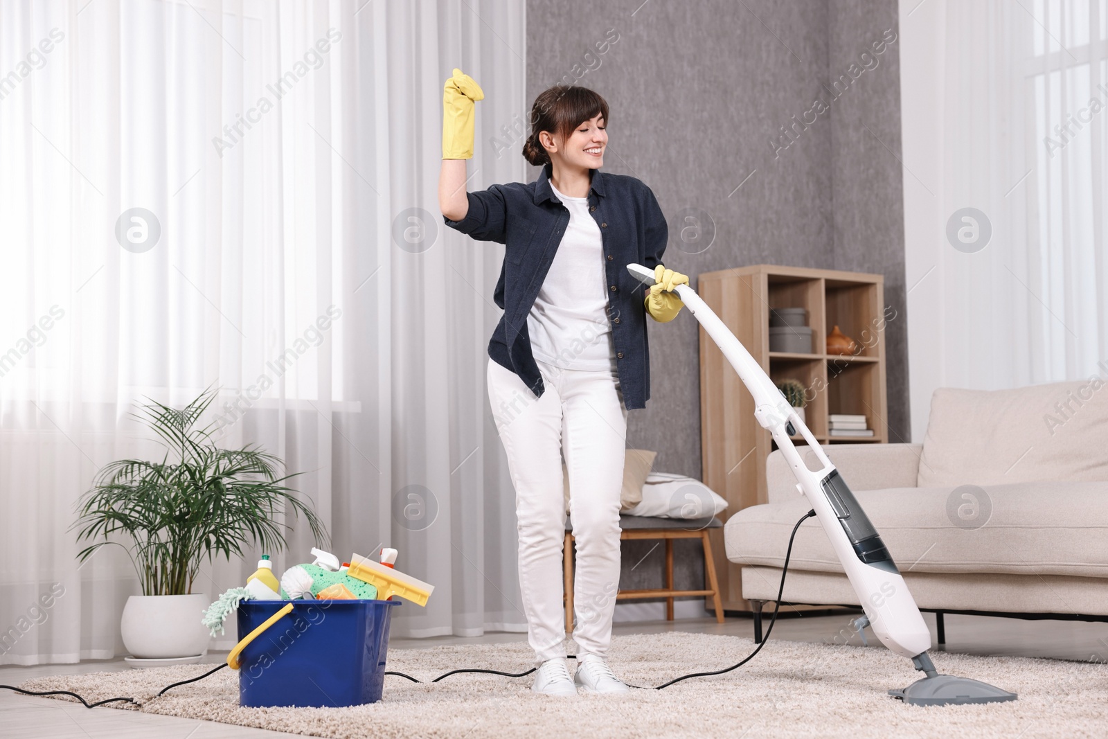 Photo of Happy young housewife having fun while cleaning carpet at home