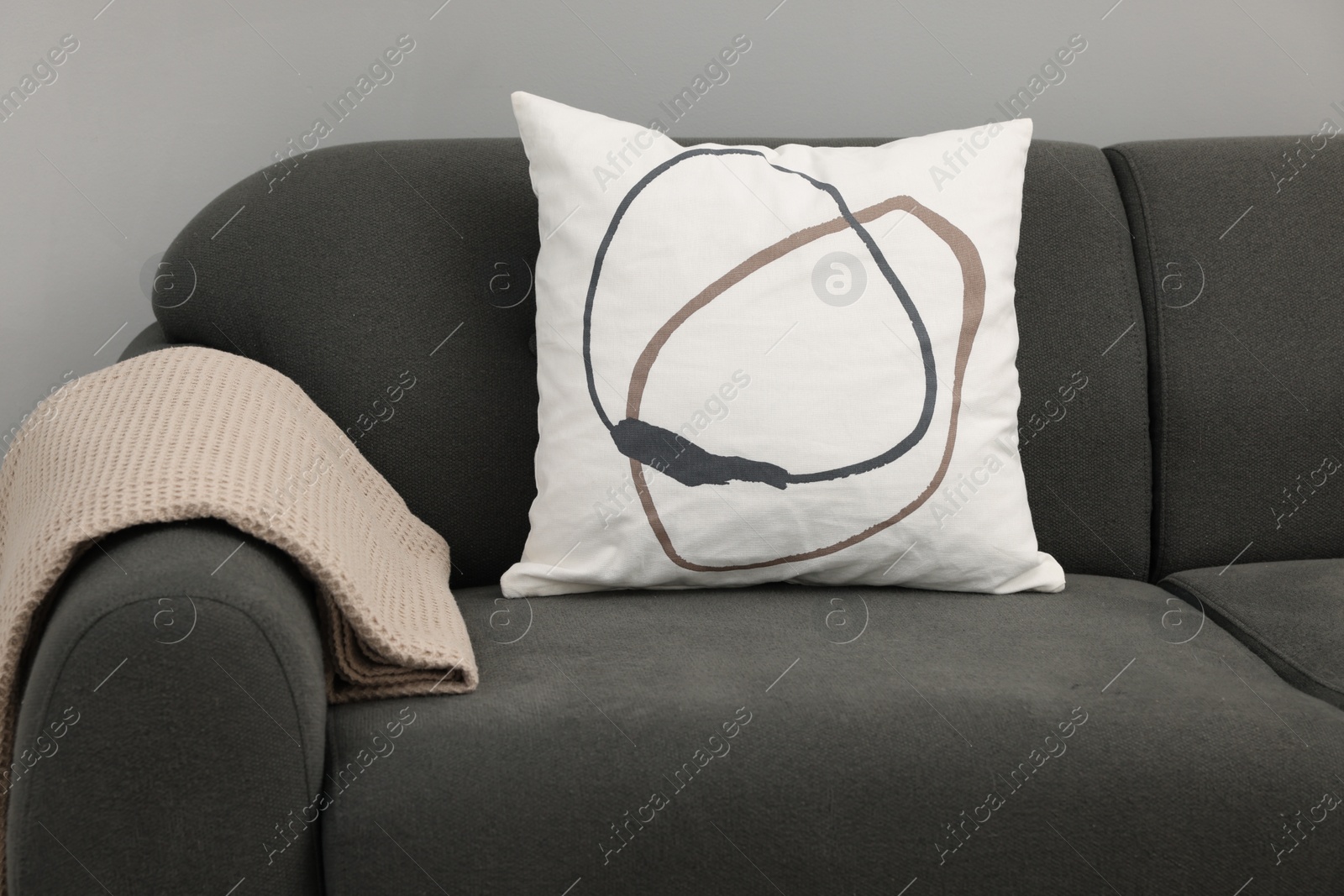 Photo of Soft pillow and blanket on sofa near grey wall indoors