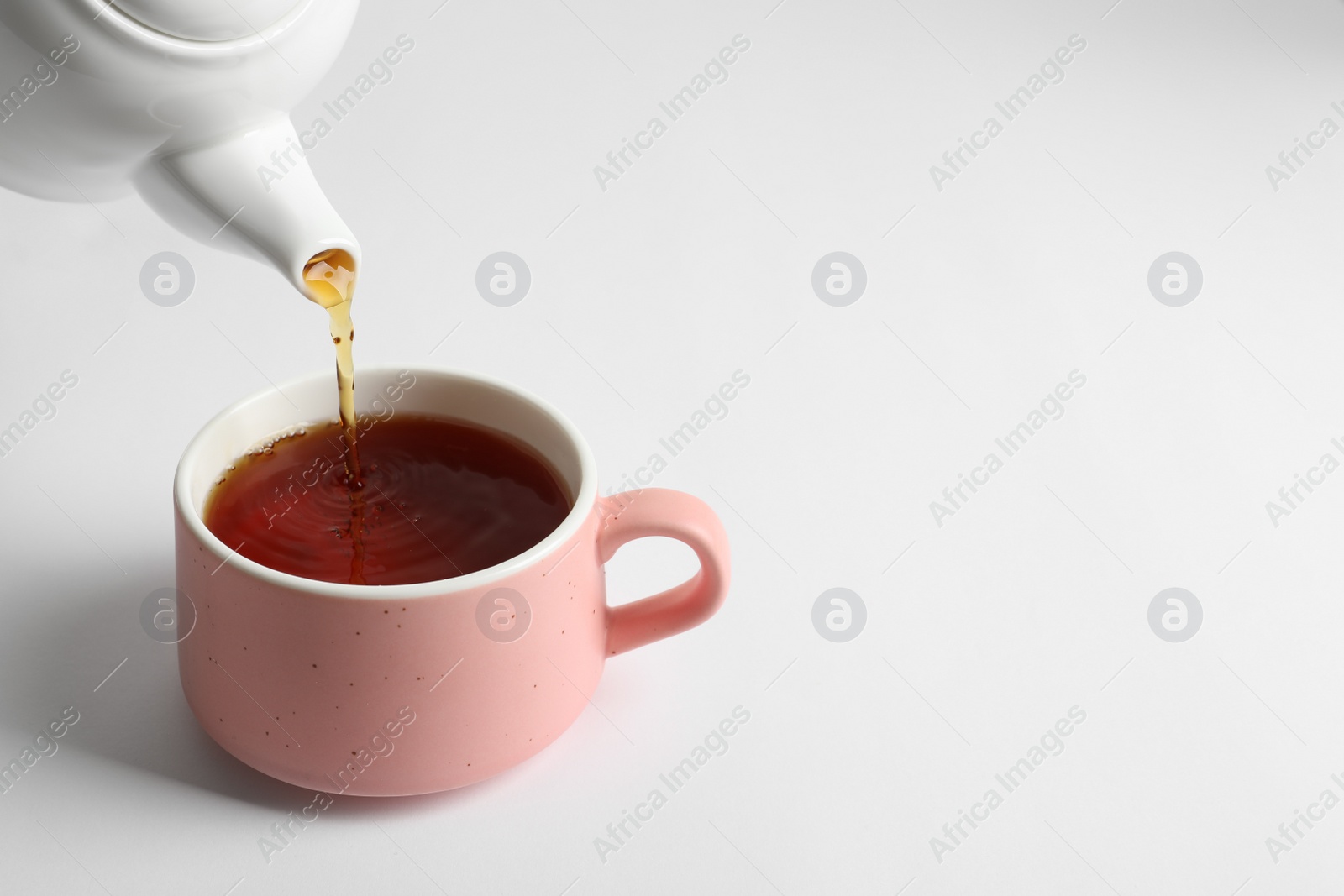 Photo of Pouring hot tea into ceramic cup on white background