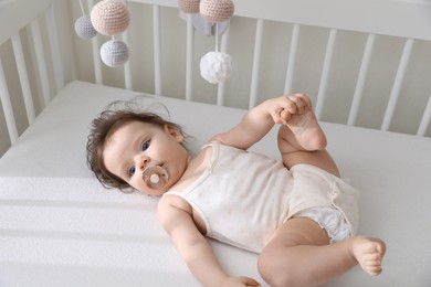 Photo of Cute little baby lying in crib with hanging mobile