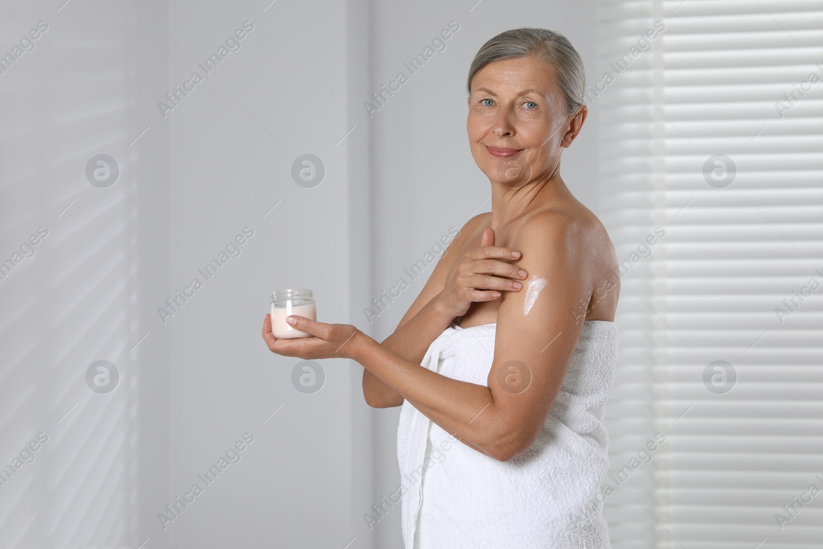 Photo of Happy woman applying body cream onto arm indoors. Space for text