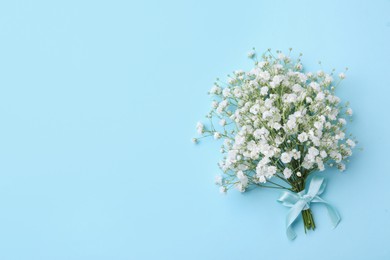 Photo of Beautiful gypsophila flowers tied with ribbon on light blue background, top view. Space for text