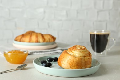 Photo of Delicious bun with blueberries, jam and coffee on white table