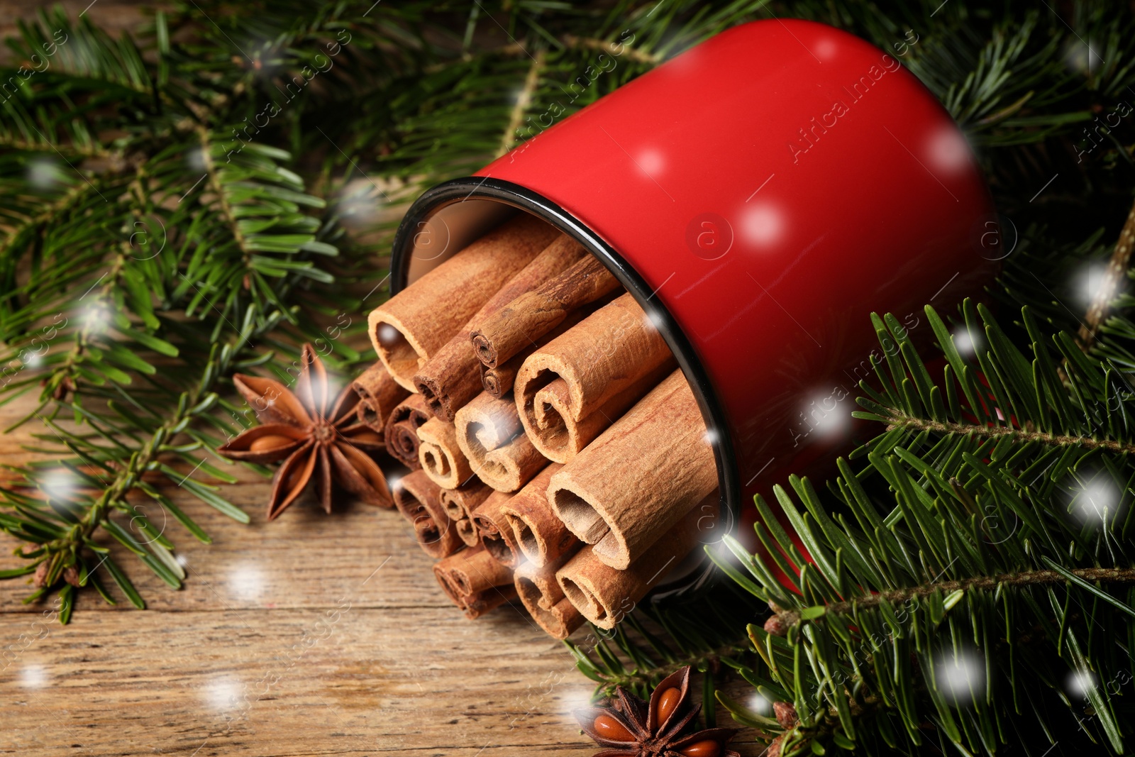 Image of Cinnamon in red mug and anise surrounded by fir tree branches on wooden table, closeup