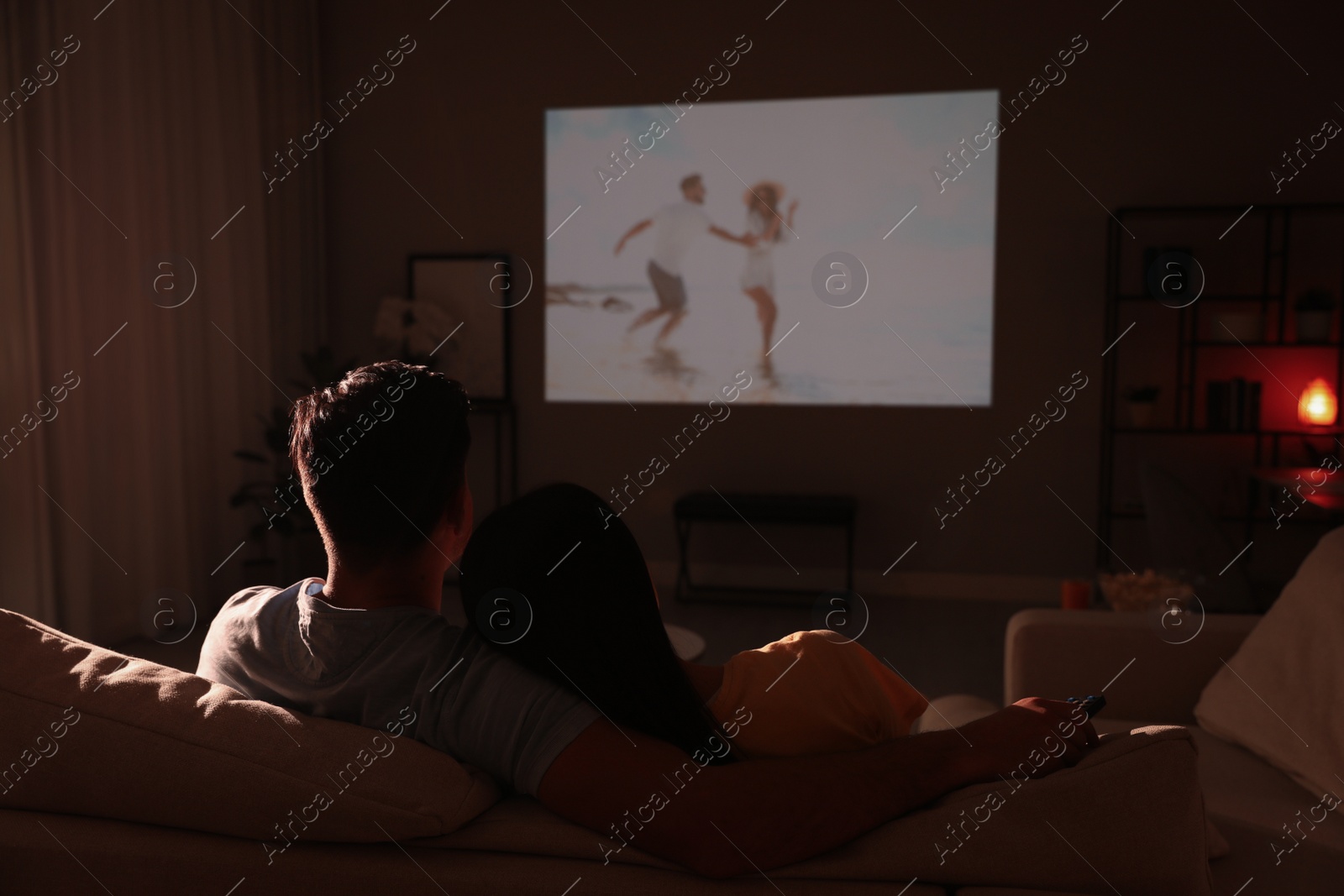 Photo of Couple watching movie on sofa at night, back view