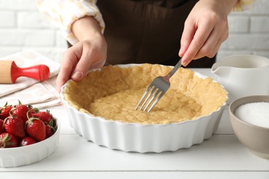 Photo of Shortcrust pastry. Woman making holes in raw dough with fork at white wooden table, closeup