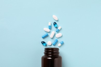Plastic bottle with many different pills on light blue background, flat lay
