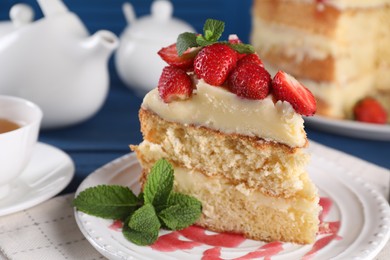 Photo of Piece of tasty cake with fresh strawberries, mint and cup of tea on table, closeup