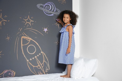 Photo of African-American child drawing rocket with chalk on wall in bedroom