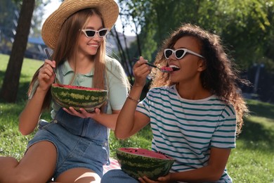 Happy girls eating watermelon on picnic blanket in park