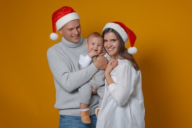 Photo of Happy couple with cute baby wearing Santa hats on yellow background. Christmas season