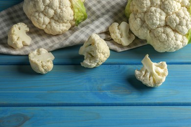 Photo of Fresh whole and cut cauliflowers on light blue wooden table. Space for text