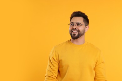 Handsome man wearing glasses on orange background, space for text