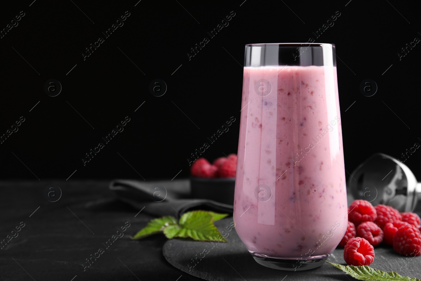 Photo of Glass of tasty raspberry smoothie on dark table against black background, space for text
