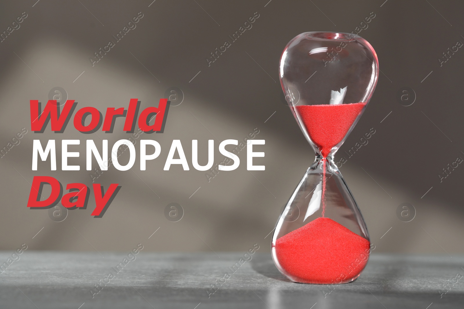 Image of World Menopause Day. Hourglass with red sand on grey table