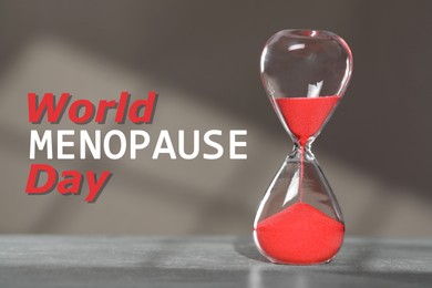 Image of World Menopause Day. Hourglass with red sand on grey table